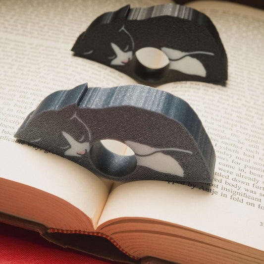 Sleepy tuxedo cat page holders resting in a book. Gray and black variations shown