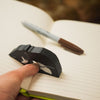 Sleepy black tuxedo cat page holder holding open a planner next to a brown permanent marker