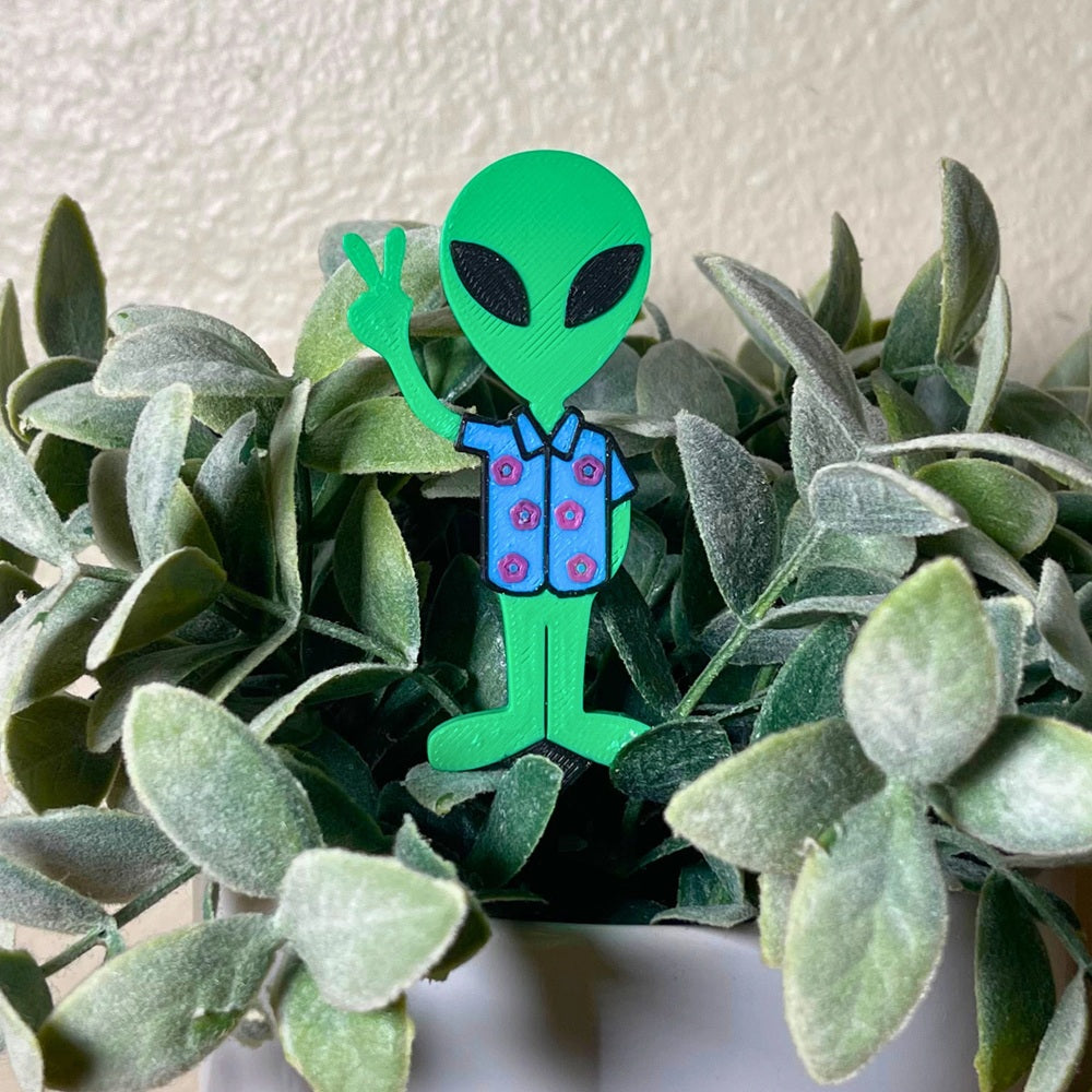 Fun alien plant stake in a Hawaiian t-shirt holding a peace sign in a houseplant