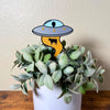 UFO Plant stake with alien inside using it's golden beam to pull up a cow stuck inside a house plant