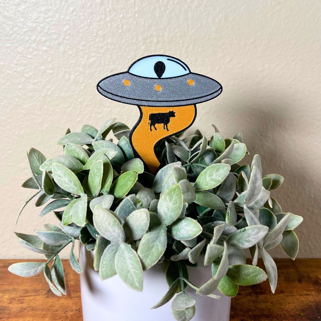 UFO Plant stake with alien inside using it's golden beam to pull up a cow stuck inside a house plant